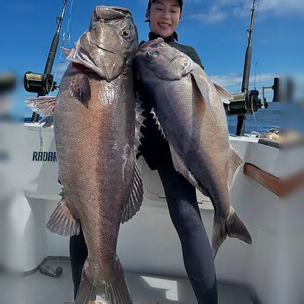 Angler on a boat holding two big hāpuku